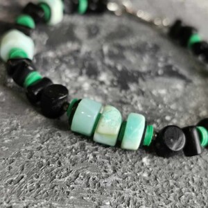 May include: A close-up of a green and black beaded bracelet. The bracelet is made with round, green beads and square, black beads.