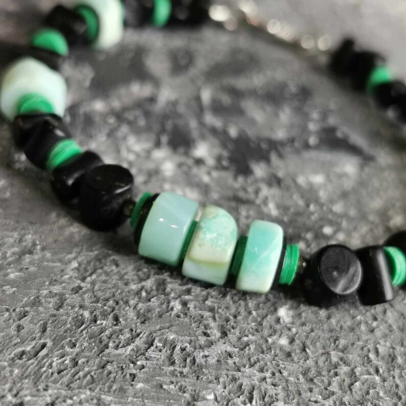 May include: A close-up of a green and black beaded bracelet. The bracelet is made with round, green beads and square, black beads.