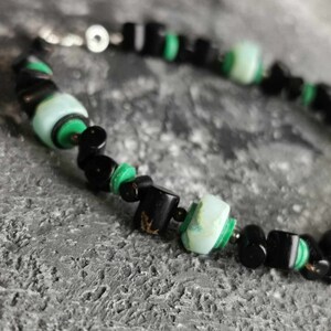 May include: A black and green beaded necklace with a silver clasp. The beads are made of black onyx and green malachite.