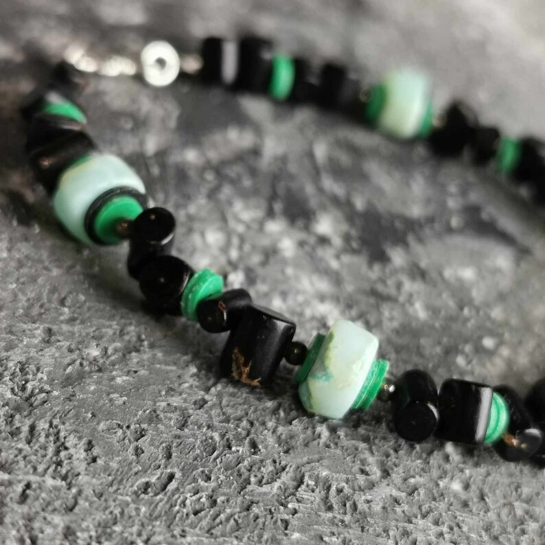 May include: A black and green beaded necklace with a silver clasp. The beads are made of black onyx and green malachite.