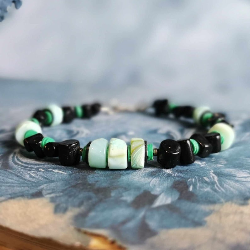 May include: A bracelet made with black, green, and white beads. The bracelet has a mix of round and rectangular beads.