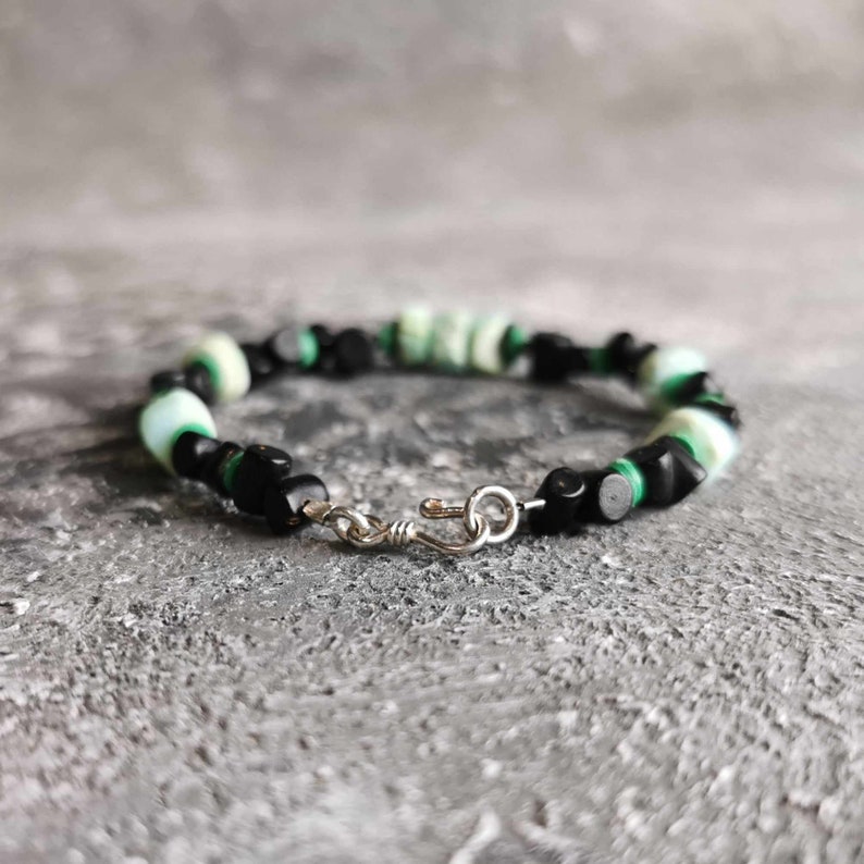 May include: A black and green beaded bracelet with a silver clasp. The bracelet is made with small, round beads and is approximately 7 inches in length.
