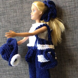 May include: A blue and white knitted outfit for a doll, including a hat, pants, top, and bag. The outfit is made with a white and blue striped pattern.