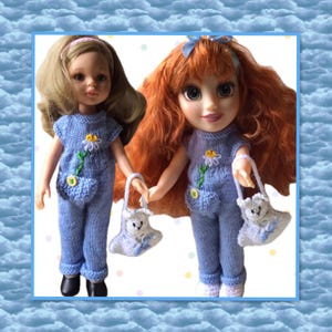 May include: Two dolls wearing matching blue knit outfits with daisy accents and small pockets. Each doll holds a white purse with a teddy bear design. One doll has blonde hair and a pink headband, the other has red hair and a blue bow.