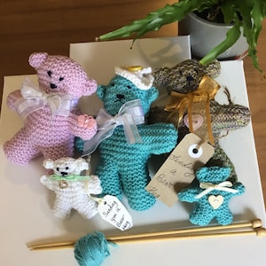Peut inclure: Cinq ours en peluche tricotés dans différentes couleurs, dont le rose, le bleu sarcelle et le marron. Les ours sont tous faits à la main et présentent des détails différents, tels que des nœuds, des boutons et des cœurs. Les ours sont disposés sur une surface blanche avec des aiguilles à tricoter et de la laine. Le texte sur l'étiquette indique "Sending you a Bear Hug."