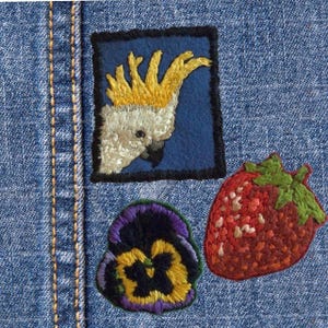 Può includere: Tre toppe ricamate su uno sfondo di denim blu. Le toppe sono un cacatua giallo e bianco, una fragola rossa e una viola viola, gialla e nera.