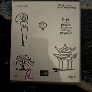 May include: A black and white stamp set with the words "Power of Hope" and images of a pagoda, a tree, a lantern, and a person holding an umbrella. The text "Good Luck" and "Today is a day for new beginnings" are also included. The set is from Stampin' Up!.