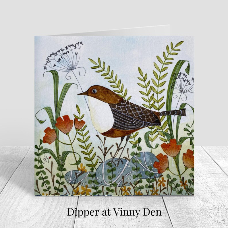 Puede incluir: Tarjeta de felicitaci&oacute;n cuadrada con una ilustraci&oacute;n a la acuarela de un p&aacute;jaro con plumas marrones y blancas, posado sobre una roca en medio de flores naranjas y follaje verde. El texto "Dipper at Vinny Den" est&aacute; impreso en la parte inferior.