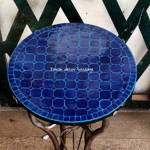 May include: A blue and white mosaic tile top table with a black metal base. The table is round and has a decorative design. The text "Farah decor soudagge" is visible on the table top.