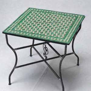 Op de afbeelding: Vierkante mozaïek tegel tafel met een groen en wit geometrisch patroon. De tafel heeft een zwart metalen frame met gebogen poten en decoratief krulwerk. De tafel is ongeveer 61 cm vierkant.