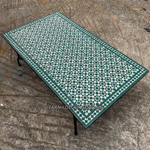 May include: A rectangular table featuring a green and white geometric mosaic tile top with a star and diamond pattern. The table has a black metal frame with thin legs and the text FARAH DECOR SOUDAGE is printed on the surface of the tabletop.