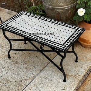 May include: A black metal folding table with a white and black mosaic tile top. The table is sitting on a stone patio.