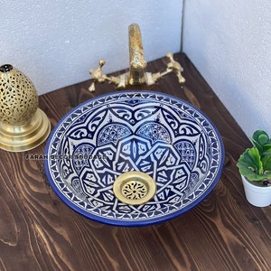 May include: A blue and white ceramic sink with intricate geometric patterns and a gold drain. The sink is on a wooden countertop.