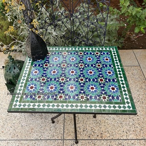 Könnte beinhalten: Ein quadratischer Tisch mit einer Mosaikplatte, die ein geometrisches Muster in Blautönen, Grün- und Rottönen aufweist. Der Tisch hat ein schwarzes Metallgestell mit vier Beinen.