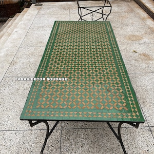 May include: A green and brown mosaic tile table top with a black metal frame. The table is on a gray tiled patio. The text "FARAH DECOR SOUDAGE" is visible on the table top.