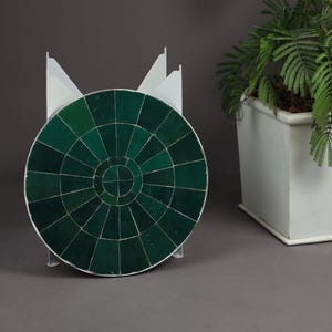 Peut inclure: Une table circulaire avec un plateau en carreaux vert foncé au motif radial et un cadre en métal blanc, placée à côté d'une grande jardinière rectangulaire blanche contenant une plante verte au feuillage délicat et plumeux.