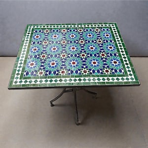 Op de afbeelding: Vierkante mozaïek tegel tafel met een decoratief patroon in tinten groen, blauw en rood. De tafel heeft een donker metalen onderstel met vier poten. Het tafelblad is ongeveer 91 cm vierkant.