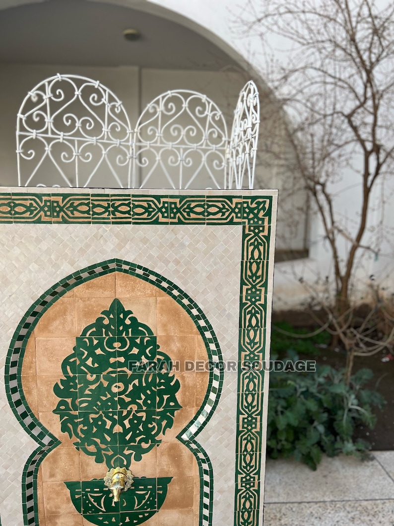 Puede incluir: Una fuente tradicional marroqu&iacute; con intrincados azulejos verdes y marrones. La fuente presenta un arco decorativo y un peque&ntilde;o ca&ntilde;o. El texto "FARAH DECOR SOUDAGE" es visible en la fuente.