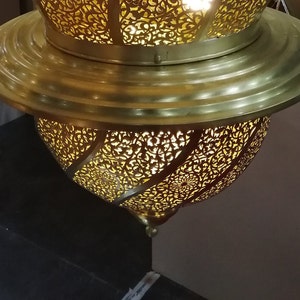 May include: A gold metal Moroccan lantern with intricate cut-out designs. The lantern has a round shape and a decorative top.