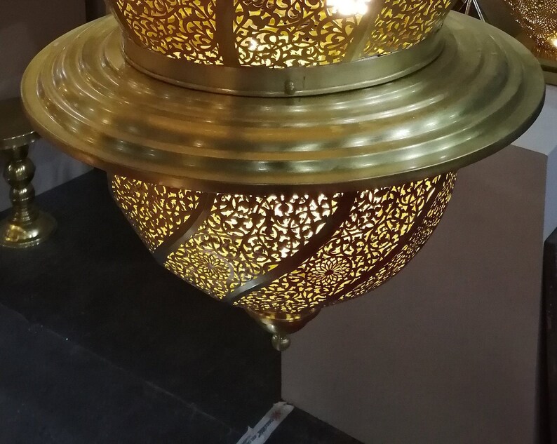 May include: A gold metal Moroccan lantern with intricate cut-out designs. The lantern has a round shape and a decorative top.
