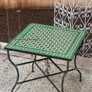 May include: A square green and beige tiled table with a black metal frame. The table has a diamond pattern and is sitting on a grey tiled floor. The text "FARAH DECOR SOUDAGE" is visible on the table.