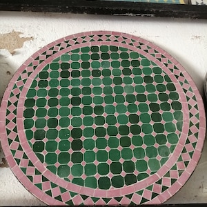 May include: A round green and pink mosaic tile table top. The table top is made of small square tiles arranged in a repeating pattern.