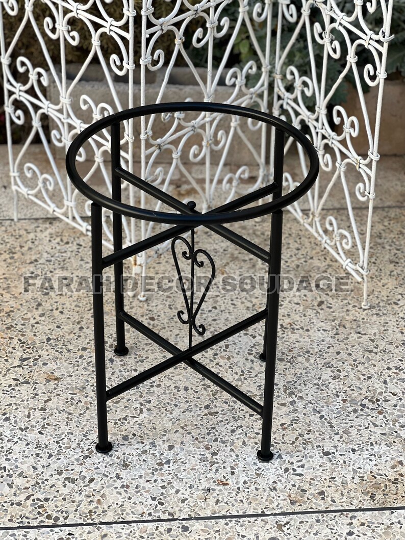 Puede incluir: Soporte de metal negro con parte superior redonda y un dise&ntilde;o decorativo de volutas. El soporte tiene un dise&ntilde;o simple y elegante y ser&iacute;a perfecto para exhibir plantas u otros art&iacute;culos decorativos.