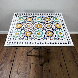 May include: A white ceramic mug with a black handle and the text "But First, Coffee" in a bold, black font. The mug is set against a blurred background, suggesting a cosy setting.