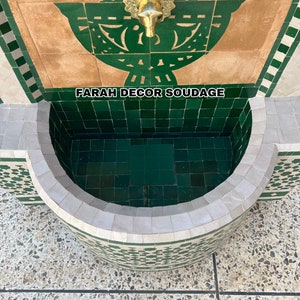 Puede incluir: Una fuente de azulejos verdes y blancos con un grifo de lat&oacute;n. La fuente tiene una cuenca curva y un dise&ntilde;o decorativo sobre el grifo. El texto "FARAH DECOR SOUDAGE" es visible en la fuente.