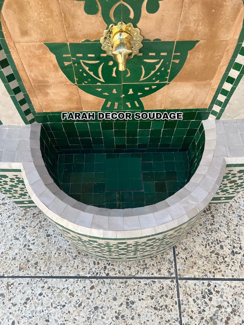 Puede incluir: Una fuente de azulejos verdes y blancos con un grifo de lat&oacute;n. La fuente tiene una cuenca curva y un dise&ntilde;o decorativo sobre el grifo. El texto "FARAH DECOR SOUDAGE" es visible en la fuente.