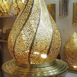 May include: A large, ornate, gold-colored metal pendant light fixture with intricate cut-out designs. The light fixture is shaped like a teardrop and has a round base.