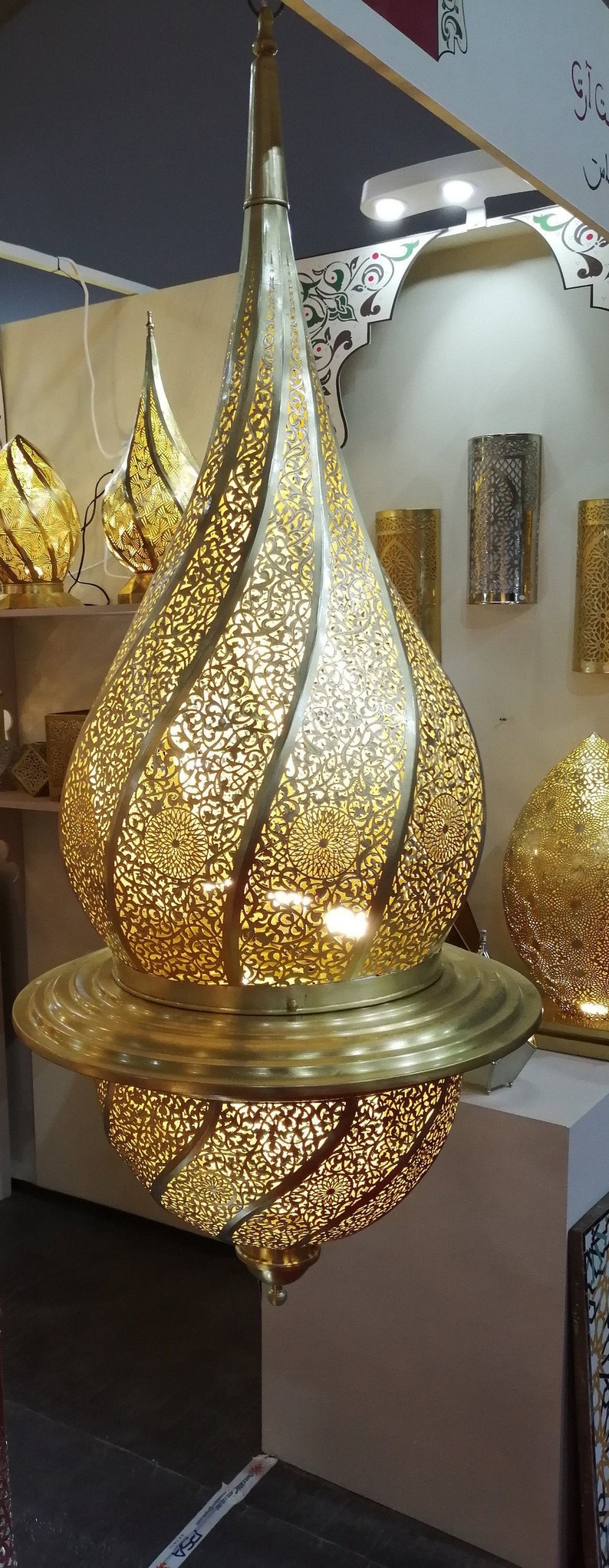 May include: A large, ornate, gold-colored metal pendant light fixture with intricate cut-out designs. The light fixture is shaped like a teardrop and has a round base.