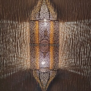 May include: A gold metal Moroccan lantern with intricate cut-out designs. The lantern is lit and casts a warm glow.Handmade Moroccan Wall Lamp | Brass Moroccan Sconce | Artisan Wall Lighting | Boho & Mediterranean Decor .