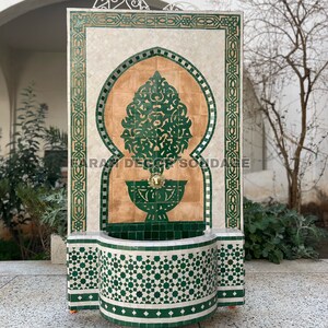 Puede incluir: Una fuente de azulejos verdes y marrones con un arco decorativo y un peque&ntilde;o ca&ntilde;o. La fuente tiene ruedas y una cuenca en la parte inferior.