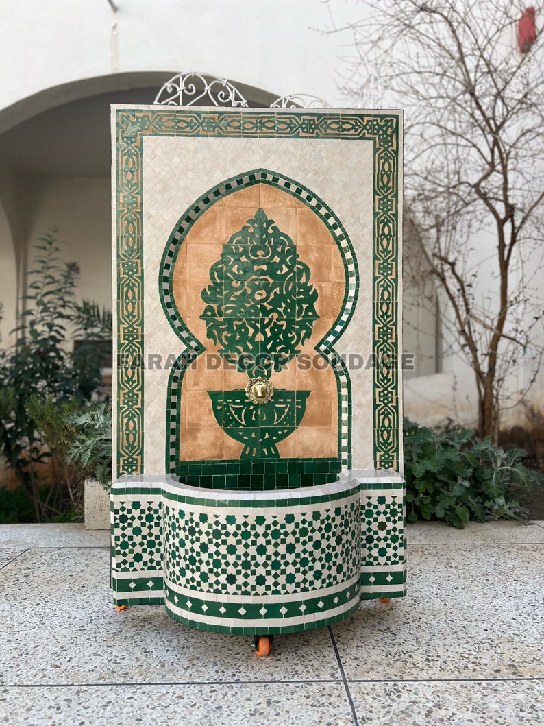 Puede incluir: Una fuente de azulejos verdes y marrones con un arco decorativo y un peque&ntilde;o ca&ntilde;o. La fuente tiene ruedas y una cuenca en la parte inferior.