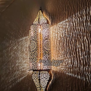 May include: A decorative wall sconce with intricate metalwork and a warm, glowing light. The sconce is made of brass and has a traditional Moroccan design.