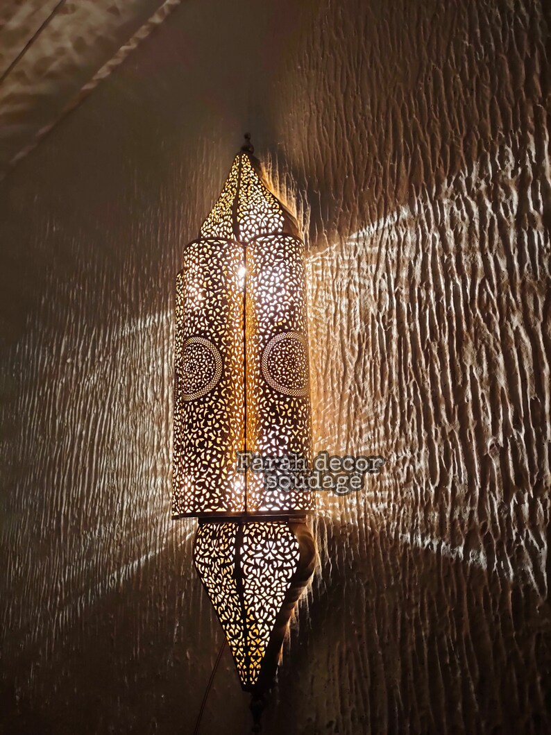 May include: A decorative wall sconce with intricate metalwork and a warm, glowing light. The sconce is made of brass and has a traditional Moroccan design.