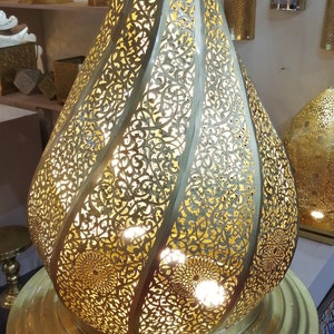 May include: A gold metal Moroccan pendant light with intricate cut-out designs. The light is shaped like a teardrop and has a round base.