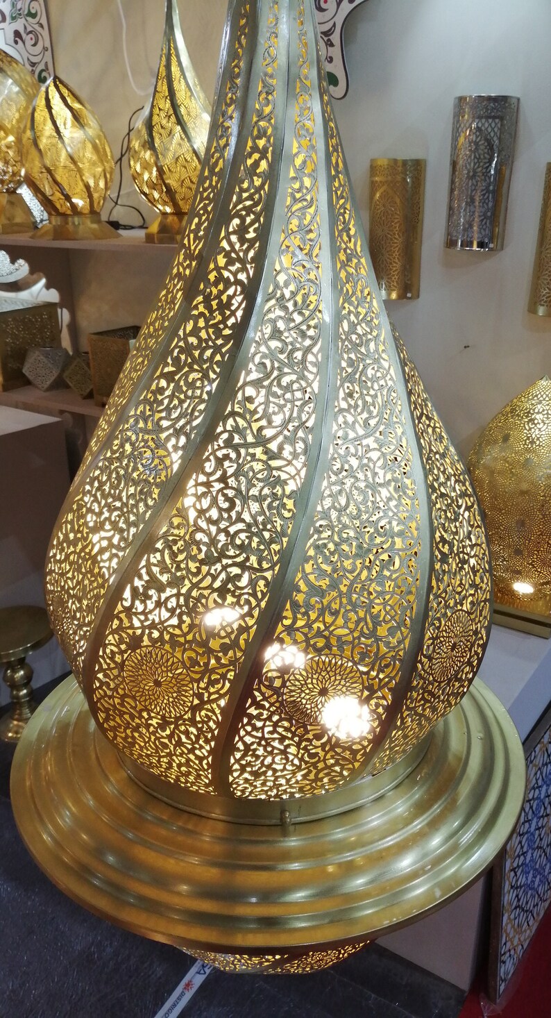 May include: A gold metal Moroccan pendant light with intricate cut-out designs. The light is shaped like a teardrop and has a round base.