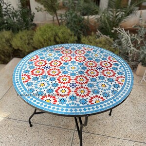 May include: A round mosaic table with a blue, red, white and yellow geometric pattern. The table has a black metal frame.