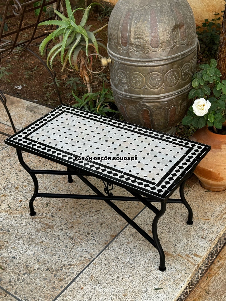 May include: A black metal folding table with a white and black mosaic tile top. The table is sitting on a stone patio. Customizable Mosaic Table - Rectangular Outdoor Indoor Zellige Tile Table With Iron Base
