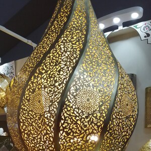 May include: A gold metal Moroccan pendant light with intricate cut-out designs. The light is shaped like a teardrop and has a warm glow.