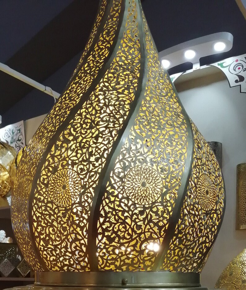 May include: A gold metal Moroccan pendant light with intricate cut-out designs. The light is shaped like a teardrop and has a warm glow.