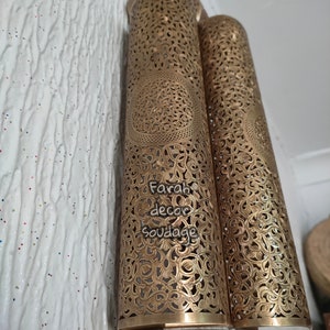 May include: Two gold metal lanterns with intricate cut-out designs. The lanterns are attached to a wall and have a decorative base.