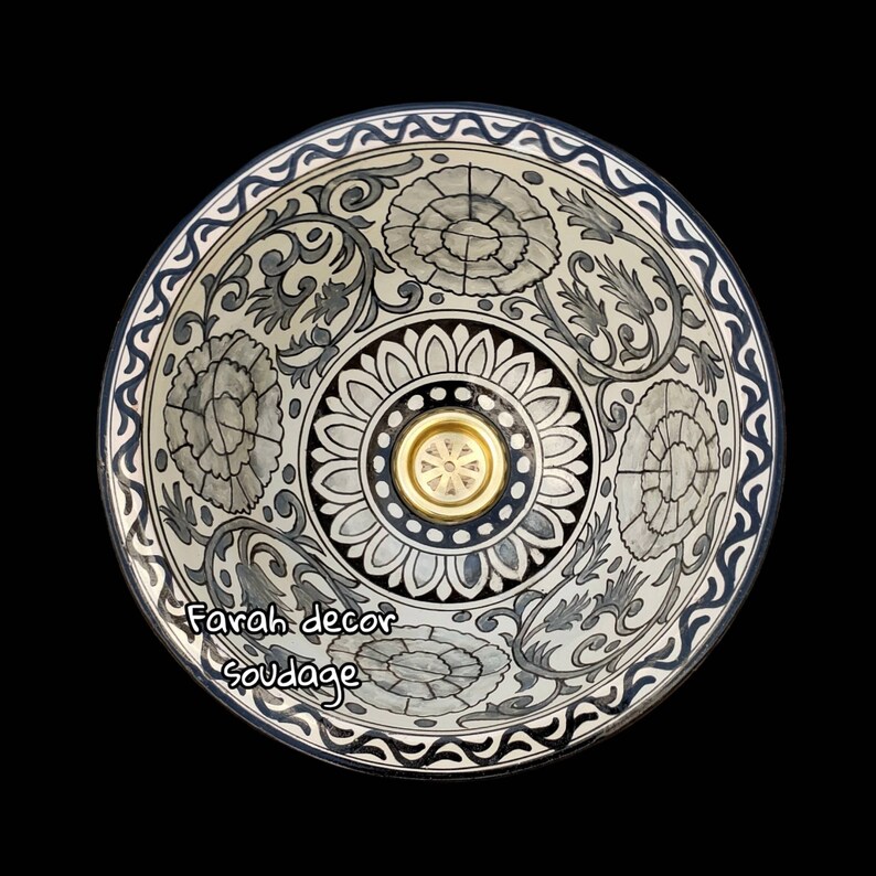 May include: A white ceramic bowl with a black and grey floral design. The bowl has a gold-coloured metal insert in the centre.