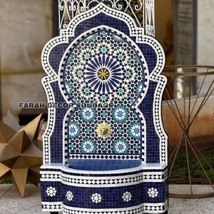 Peut inclure: Une fontaine murale en mosaïque bleue et blanche avec un motif marocain traditionnel. La fontaine a un petit bassin et un bec verseur pour l'eau. Elle est sur roulettes et possède une arche décorative.
