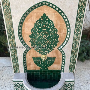 Puede incluir: Una fuente de azulejos verdes y blancos con un arco decorativo y un grifo. La fuente tiene una peque&ntilde;a cuenca en la parte inferior y est&aacute; hecha de azulejos de cer&aacute;mica.