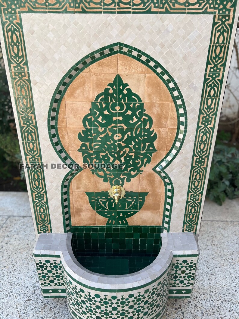Puede incluir: Una fuente de azulejos verdes y blancos con un arco decorativo y un grifo. La fuente tiene una peque&ntilde;a cuenca en la parte inferior y est&aacute; hecha de azulejos de cer&aacute;mica.