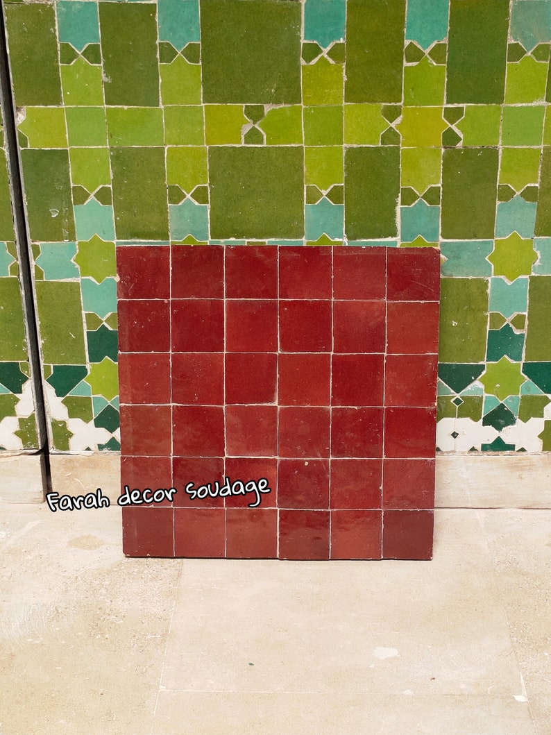 May include: A close-up of a red tile with a grid pattern. The tile is made of ceramic and has a glossy finish. The tile is part of a larger mosaic pattern. The text "Farah decor soudage" is written on the tile.