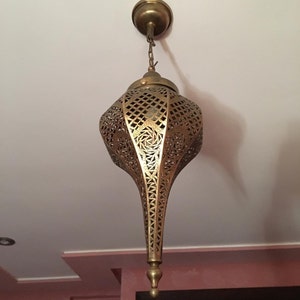 May include: A gold metal pendant light fixture with intricate cut-out designs. The light fixture is shaped like a teardrop and hangs from a chain.
